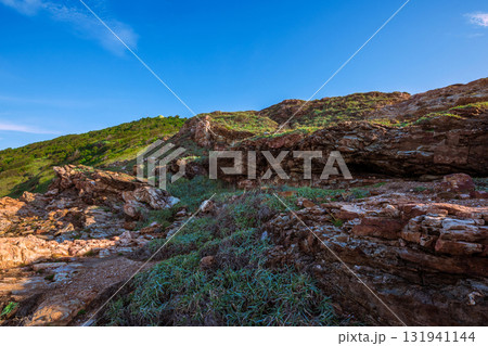 Close-up of rugged red and brown coastal rocks at Khao Laem Ya, Rayong, Thailand, contrasting with the bright blue sky and lush green slopes Close-up of rugged red and brown coastal rocks at Khao Laem Ya, Rayong, Thailand, contrasting with the bright blue sky and lush green slopes 131941144