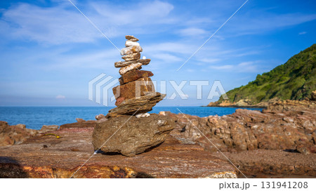 Zen rock stack or cairn balanced on the rugged coastal rocks at Khao Laem Ya, Rayong, Thailand, with the blue ocean and sky in the background 131941208