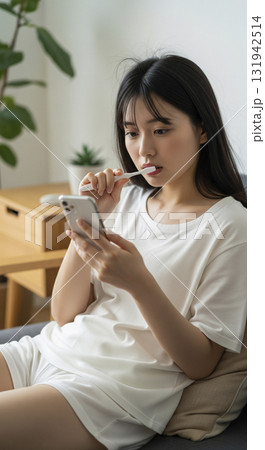 朝。ソファに座り、スマホを見ながら歯磨き 131942514