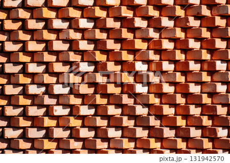 Stacked red clay bricks create a repeating textured wall with angular shadows. Urban materiality, geometric texture, construction elements, light and form Stacked red clay bricks create a repeating textured wall with angular shadows. Urban materiality, geometric texture, construction elements, light and form 131942570