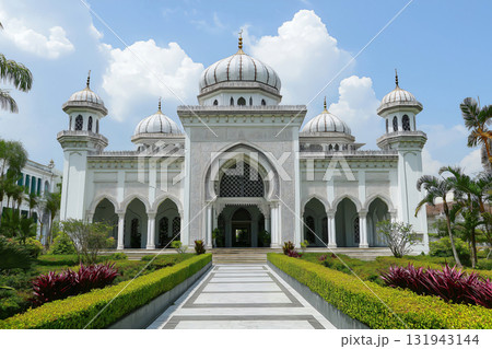 White mosque featuring Islamic architecture with a paved walkway leading to the entrance surrounded by manicured hedges 131943144