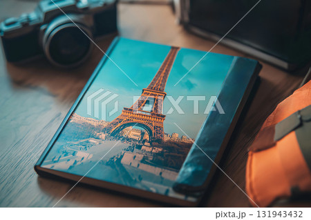 Travel guide featuring the Eiffel tower is lying on a table next to cameras and a backpack, suggesting an upcoming trip to Paris 131943432