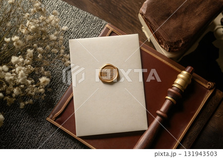 Cream colored invitation with gold wax seal displayed on a leather book, accompanied by dried flowers and a wax seal stamp, creating a vintage and elegant wedding stationery mockup 131943503