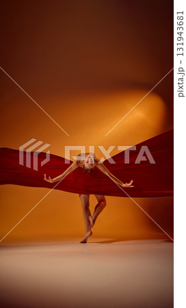 Ballet dancer bending forward in red fabric under dramatic orange lighting 131943681