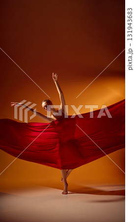 Female ballet dancer in red fabric performing balanced pose in warm light 131943683