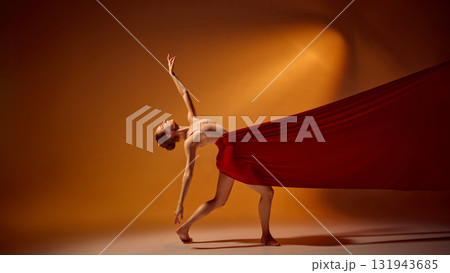 Ballet dancer bending backward in red fabric under warm orange light 131943685