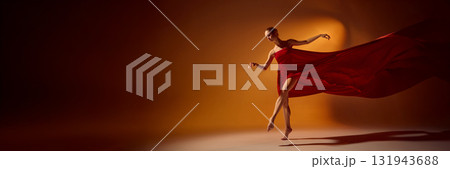 Ballet dancer in red flowing dress performing dynamic motion under orange lighting. Banner 131943688