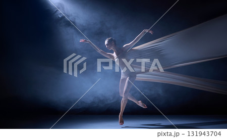 Ballet dancer in fabric performing elegant leap under blue haze light 131943704