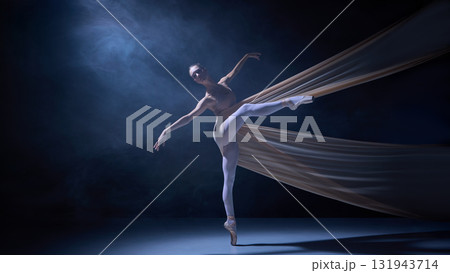 Ballet dancer standing en pointe wrapped in fabric under blue stage light 131943714