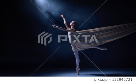 Ballet dancer in spotlight stretching arm in emotional elegance tangled in flowing fabric Ballet dancer in spotlight stretching arm in emotional elegance tangled in flowing fabric 131943721