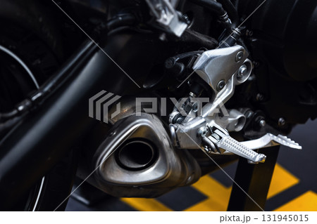 A detailed close-up of a motorcycles foot pegs, shifter, and exhaust A detailed close-up of a motorcycles foot pegs, shifter, and exhaust 131945015