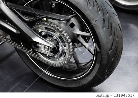 A detailed closeup of a motorcycle rear wheel, chain, sprocket, and tire 131945017