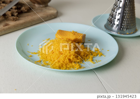 a piece of whole cheese and a large amount of finely grated yellow cheese made from milk, grating fresh orange cheese for pizza or pasta a piece of whole cheese and a large amount of finely grated yellow cheese made from milk, grating fresh orange cheese for pizza or pasta 131945423