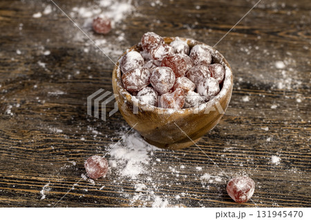 kumquat and powdered white sugar in a bowl, sweet dried orange kumquat fruits are placed in a wooden bowl and sprinkled with powdered white beet sugar 131945470