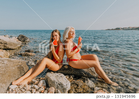 Watermelon Beach Summer: Two Women Enjoying Refreshing Watermelon Slices on Rocky Coastline 131945696