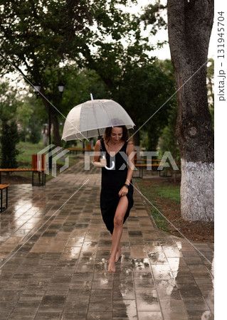Woman, Rain, Umbrella, barefoot woman walking on wet park path holding a clear umbrella, enjoying refreshing weather 131945704