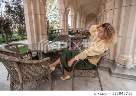 Woman Coffee Terrace - A woman sits at a table on a terrace outside a building, drinking coffee. 131945719
