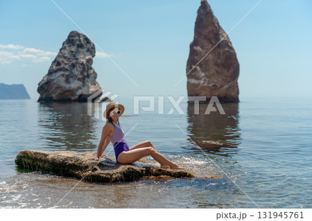 Woman ocean rocks relaxing on a coastal rock with impressive sea stacks and blue sky copy space 131945761