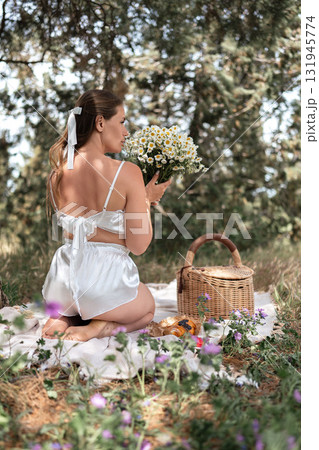 Picnic flowers woman: Summer picnic in forest, woman holds chamomile bouquet, enjoying peaceful outdoor moment. 131945774