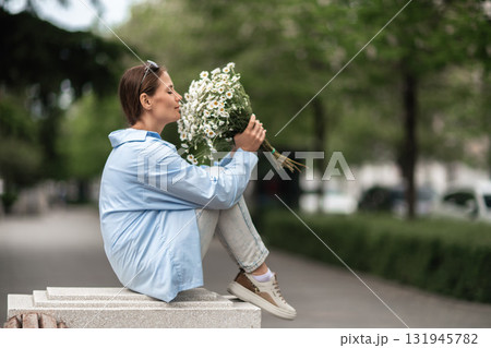 Daisies Bouquet Woman: Sits on bench in park, closes eyes, enjoys flowers scent in springtime daylight. 131945782