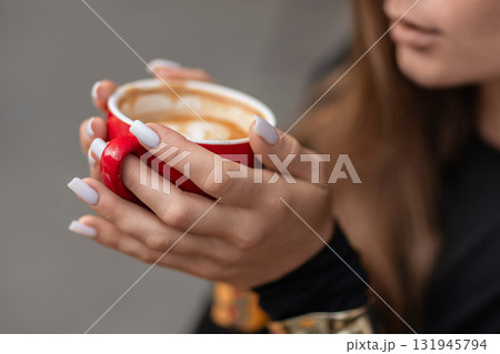 Coffee nails woman: Afternoon beverage break - latte drink in red mug held closely by manicured hands. 131945794