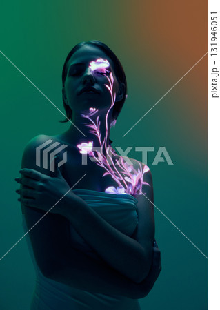 Woman with glowing floral projection on face and chest in dark gradient lighting Woman with glowing floral projection on face and chest in dark gradient lighting 131946051