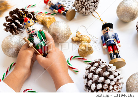 Child hands holding nutcracker among festive Christmas ornaments and pinecones Child hands holding nutcracker among festive Christmas ornaments and pinecones 131946165