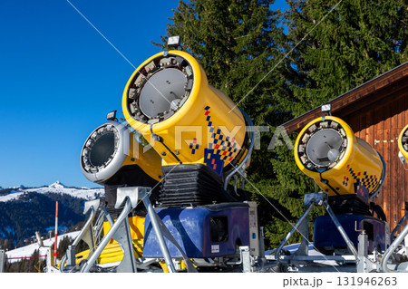 Operating artificial snow cannon near piste making snowy powder.Ski lift ropeway on hilghland alpine mountain winter resort on bright sunny day. downhill slopes with people enjoy sport activities Operating artificial snow cannon near piste making snowy powder.Ski lift ropeway on hilghland alpine mountain winter resort on bright sunny day. downhill slopes with people enjoy sport activities 131946263