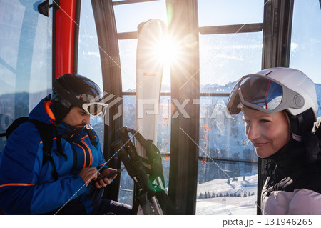Scenic two skiers study trail map inside ski lift gondola at warm sunrise light at mountain alpine resort. Scenery group friends teamwork, planning, and excitement downhill winter sports adventure Scenic two skiers study trail map inside ski lift gondola at warm sunrise light at mountain alpine resort. Scenery group friends teamwork, planning, and excitement downhill winter sports adventure 131946265