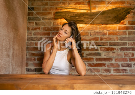 A reflective and thoughtful woman enjoys a warm phone conversation in a cozy, rustic environment, surrounded by charm A reflective and thoughtful woman enjoys a warm phone conversation in a cozy, rustic environment, surrounded by charm 131948276