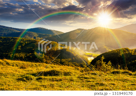 countryside mountain landscape in autumn at sunset. rural field on green hills. beautiful scenery with grassy meadows and forested slopes in highland under blue sky. scenic view in evening light 131949170