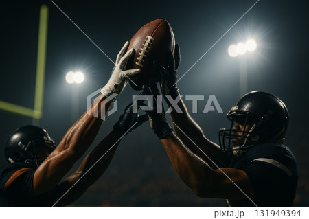 American football players reaching for ball under stadium lights, action concept American football players reaching for ball under stadium lights, action concept 131949394