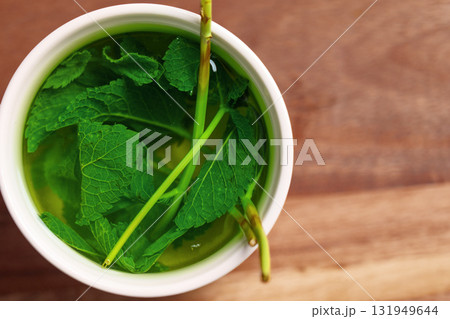 Fresh mint in mug of hot water on wooden table. Healing soothing herbal tea brewing 131949644