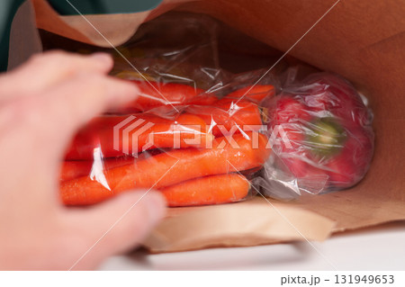 A consumer hand reaches for a paper bag full of purchased vegetables. Raw carrots and red bell peppers. A consumer hand reaches for a paper bag full of purchased vegetables. Raw carrots and red bell peppers. 131949653
