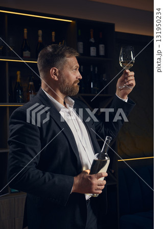 Sommelier examining clarity of white wine under warm light 131950234