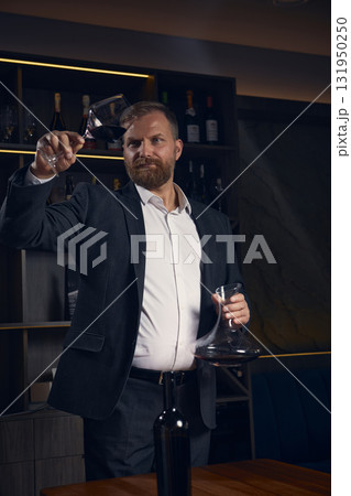 Sommelier evaluating wine color and clarity under soft light 131950250