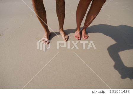 Couple standing barefoot on sandy beach with sunlit shoreline and gentle waves during a warm summer day 131951428