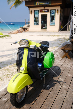 Colorful vintage scooter parked on wooden deck near sandy beach with clear blue water and tropical setting during a sunny day in warm climate 131951442