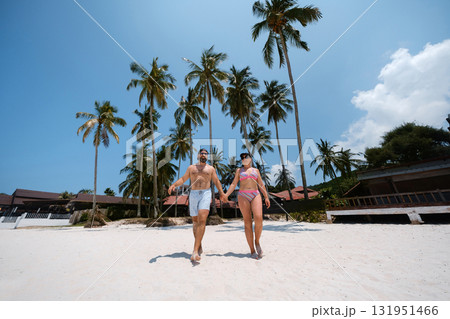 A couple strolls hand in hand along a sunny beach surrounded by palm trees near a tropical resort on a bright summer day. Redang Island. Malaysia 131951466