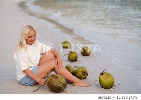 A girl is sitting on a tropical beach with coconuts in the morning enjoying the sunrise on Redang Island. Malaysia 131951478