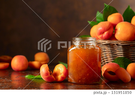 Apricot jam in jar and fresh fruits on a brown table. 131951850