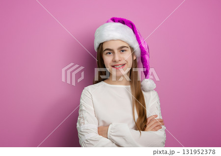 Portrait of smiling girl in pink Santa hat and white shirt pointing up on pink background. Portrait of smiling girl in pink Santa hat and white shirt pointing up on pink background. 131952378