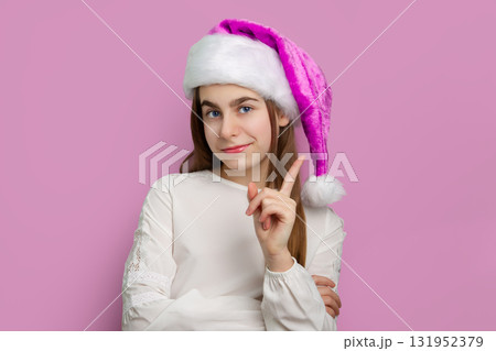 Portrait girl in pink Santa hat and white shirt pointing up on pink background. Christmas celebration and winter holiday concept. Portrait girl in pink Santa hat and white shirt pointing up on pink background. Christmas celebration and winter holiday concept. 131952379