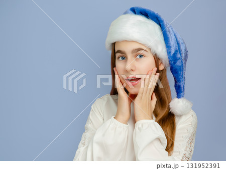 Smiling girl wearing blue and white Santa hat making heart shape with her hands,  131952391