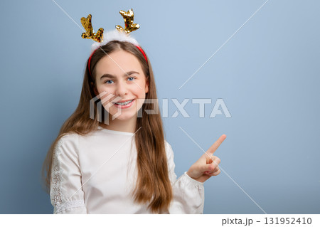 Smiling girl with sequin reindeer antlers pointing up on white background.  131952410