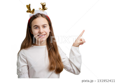 Smiling girl with sequin reindeer antlers pointing up on white background.  131952411