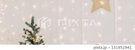 Decorated Christmas tree with shiny ornaments and fairy lights beside a wall with glowing bokeh. Festive holiday season interior design. 131952941