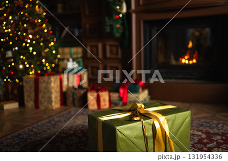 Green gift box in classical Christmas decorated interior living room library with fireplace. Christmas gift near fir tree on Christmas eve. Modern classic style interior design apartment. Christmas Green gift box in classical Christmas decorated interior living room library with fireplace. Christmas gift near fir tree on Christmas eve. Modern classic style interior design apartment. Christmas 131954336