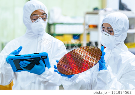 半導体工場でタブレットを持ってシリコンウエハーを検査する防護服を着た男女作業員 半導体工場でタブレットを持ってシリコンウエハーを検査する防護服を着た男女作業員 131954562
