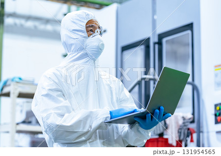 ノートパソコンを持って工場で作業する防護服を着た男性作業員 131954565